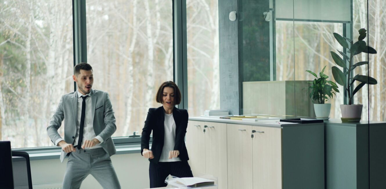 Zwei Mitarbeitende tanzen lachend im Büro – Bewegungspause staerkt Teamgeist und Gesundheit