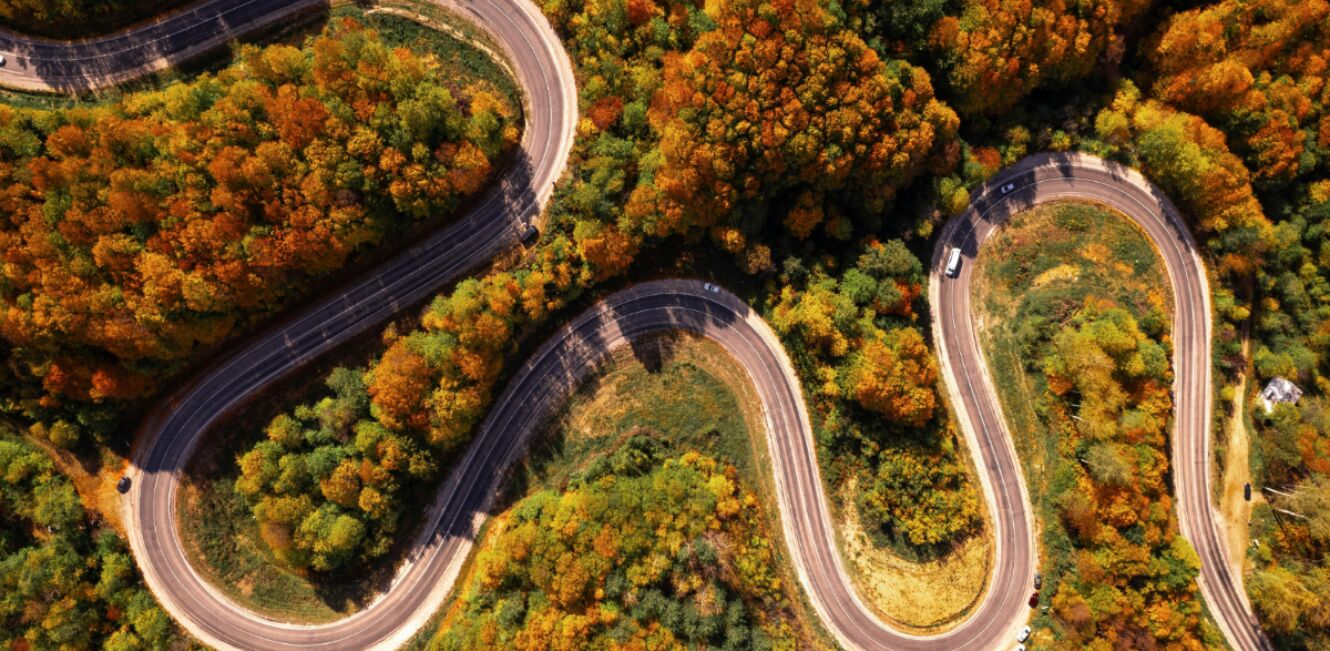 Luftaufnahme einer kurvigen Serpentinenstraße durch einen herbstlichen Wald.